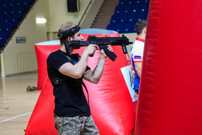 Боец LASERWAR наводит прицел на противника у красного укрытия.